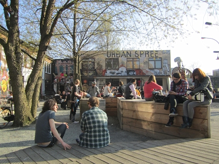 Menschen sitzen bei schönem Wetter außerhalb des Berliner Veranstaltungszentrums "Urban Spree".