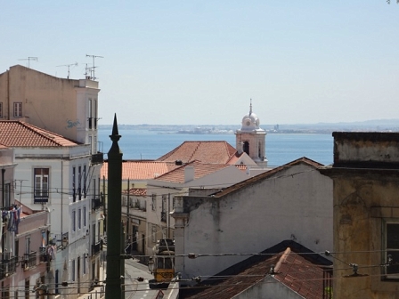 Lissaboner Gässchen mit Straßenbahn und Ausblick aufs Meer.