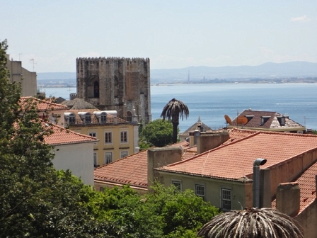 Lissabon: Häuserdächer, ein kleines Fort, eine Palme und das Meer.