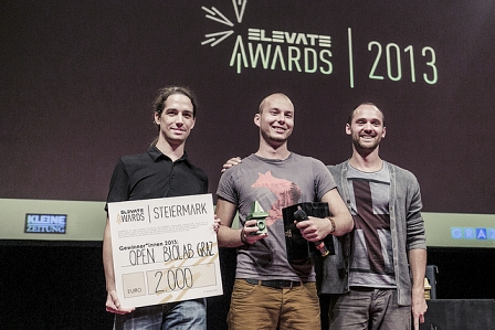 Open Biolab Graz, das Gewinnerprojekt des Steiermark Awards, hält seinen Scheck auf der Bühne der Elevate Award Show in die Kamera.