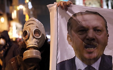 A Turkish protestor wearing a gas mask holds a banner with a portrait of Turkish Prime Minister Recep Tayyip Erdogan during an anti-government protest in Istanbul, Turkey, 27 December 2013