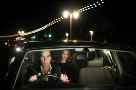 Nick Cave sitzt am Steuer eines Autos und chauffiert Kylie Minogue