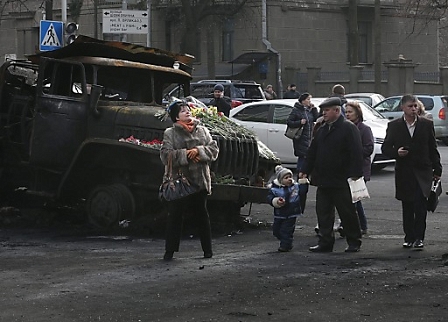 Eine Familie in der Ukraine geht auf der Straße neben einem verbrannten LKW vorbei.