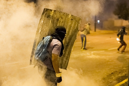 Tränengas und ein Demonstrant mit einem Schild in Venezuela