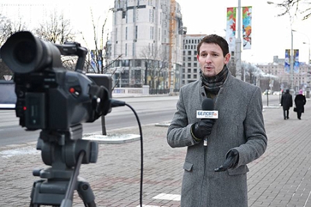 Mann steht mit Mikrophon vor einer Kamera an einem öffentlichen Platz