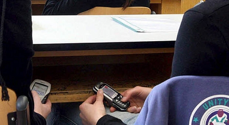 Schüler mit Handy unter der Schulbank