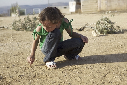 Ein kleines Mädchen schreibt etwas in den sandigen Boden in der Westbank. 