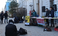 Protestkundgebung vor dem Gericht in Wiener Neustadt mit Infostand und Aktivisten davor. Am Infostand hängen Protestplakate gegen Abschiebung und die Kriminalisierung von Migration.