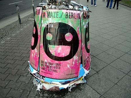 Das A MAZE.-Plakat auf einer Litfasssäule: ein schwarzes Smilyface auf buntem Hintergrund.