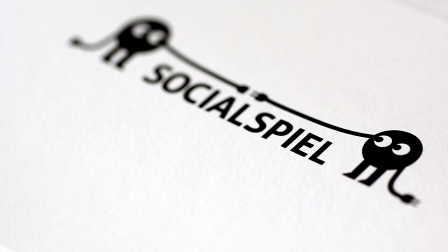 Logo von Socialspiel: runde, schwarze Smilies mit Beinen und Armen mit Stecker-Händen, die sich die Hände reichen. Dazwischen der Schriftzug in schwarzen Lettern.