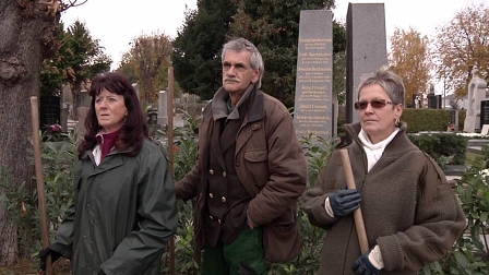 Drei Menschen stehen auf einem Friedhof zwischen Gräbern