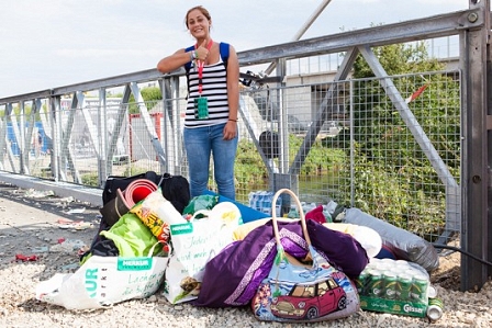 Frau steht inmitten von Gepäck, Sackerln, Koffer und Getränkekisten auf einer Brücke