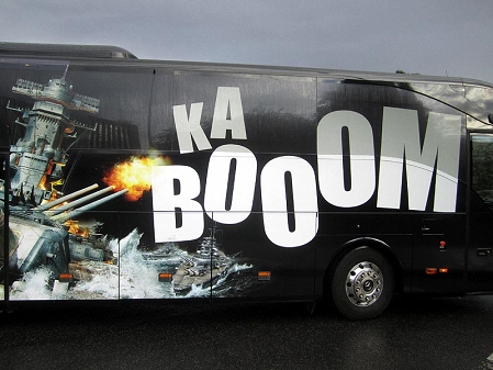 Ein Bus, der mit einem Schlachtschiff gebrandet ist, daneben steht in riesigen Lettern "KABOOM".