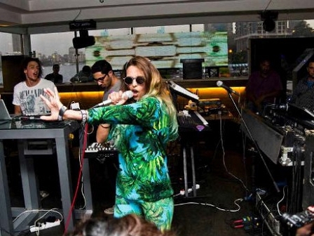 Frau in grünem Outfit sing vor zwei DJs in ein Mikro