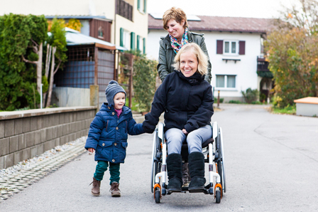 Sabrina Nitz im Rollstuhl, ihr zweijähriger Sohn und ihre persönliche Assistentin auf der Straße