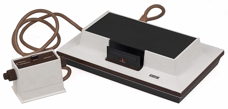 "Magnavox Odyssey": Eine Videospielkonsole in schwarz und weiß mit einem altertümlich anmutenden Drehregler und einem dicken roten Kabel.