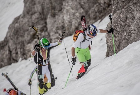 Drei Männer stapfen mit Tourenschi auf dem Rücken durch den SChnee einen Berg hinauf