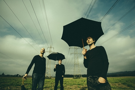 Portraitfoto das Trio The Base mit Regenschirmen