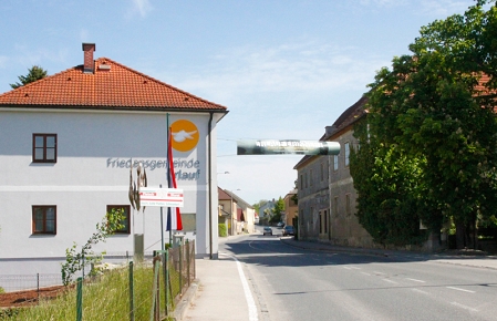 Inschrift "Friedensgemeinde Erlauf" auf einem hellblauen Haus, davor iene Fahne.