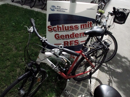 Ein Rad der Technischen Universität Graz und daneben ein Plakat des Ring Freiheitlicher Studenten mit dem Slogan "Schluss mit Gendern"