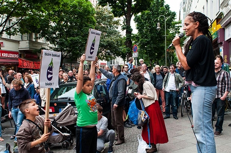 Ein frau hält eine rede für das Bizim Bakkal, Kinder halten Schilder mit der Aufschrift "bizim Bakkal bleibt"