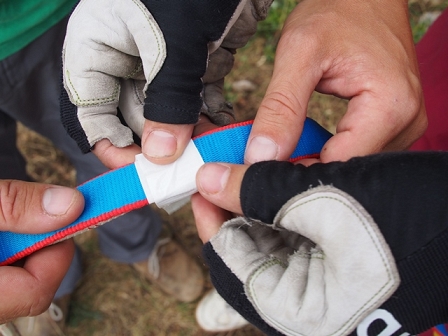 Großaufnahme: Hände verbinden Slackline und Sicherung mit einem Klebeband