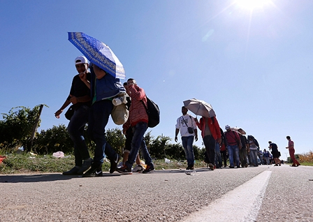 Flüchtlinge mit Sonnenschirmen auf einer Asphaltstraße