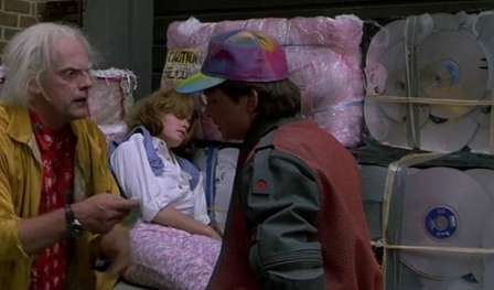 Doc Brown, Marty McFly und Jennifer Parker vor eonem Stapel alter Laserdiscs & CDs.