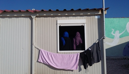 Zwei Frauen mit Kopftuch von hinten durch ein Fenster in einen Container fotografiert. DAvor Wäsche
