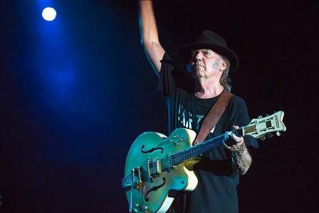 Der alte Neil Young auf der Bühne mit Gitarre reckt eine Hand nach oben