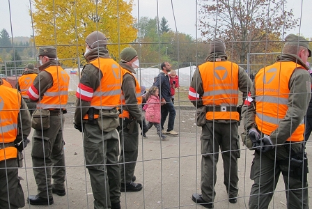 Ankunft in Österreich: Mann mit zwei Kindern betritt österreichisches Staatsgebiet, an Trennzaun stehen Soldaten