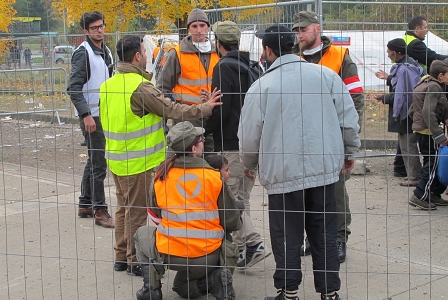 Soldatin mit einem Flüchtlingsbuben, um sie herum stehen weitere Soldaten, ehrenamtlicher Dolmetscher und ein erwachsener Flüchtling im Transitbereich in Spielfeld 