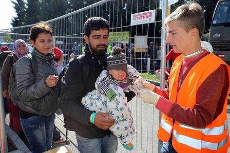 Ehrenamtlicher in Tarnweste gibt Flüchtlingen Armband, der Flüchtling trägt ein Baby