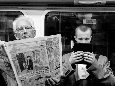 Zwei Männer in der Ubahn, einer liest eine Zeitung, der andere tappt am Tablet.