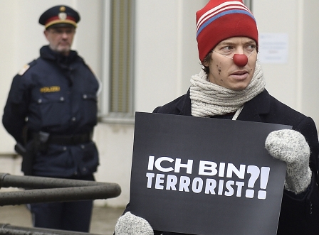 Mann mit Schild "Ich bin Terrorist?!" beobachtet von Polizist