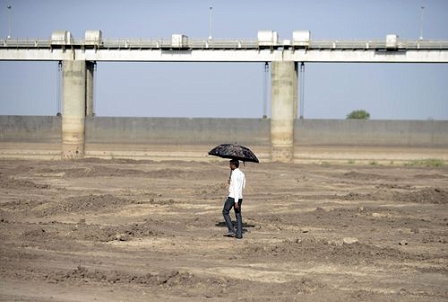 Global Warming: An Indian man holds an umbrella as he walks on the dry reservoir bed next to Gunda Dam by Gunda village in Botad district.