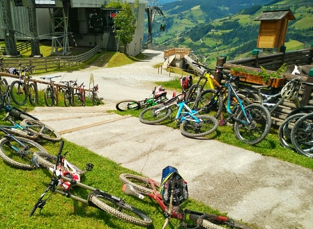 Etliche Fahrräder liegen links und rechts eines Weges zwischen Liftstation und Schihütte. Im Hintergrund der Startturm des Downhilll-Trails.