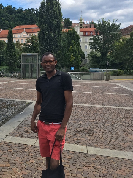 Fiston Mwanza Mujila am Grazer Mariahilferplatz, hinter ihm sieht man den Schloßberg, auf dem Fiston ein Jahr als Stadtschreiber im Cerrini Schlössl gelebt hat