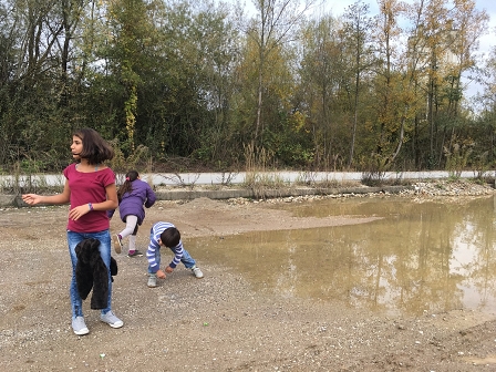 Zwei syrische Mädchen und ihr Bruder spielen bei einer Lache in Ljubljana, Steine über Wasser flitzen zu lassen